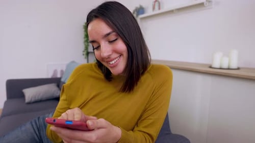 Smiling Woman Using Smartphone on Couch at Home