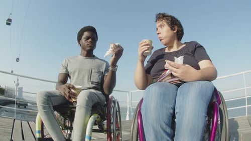 Happy Couple Using Wheelchairs Eating and Talking Outdoors
