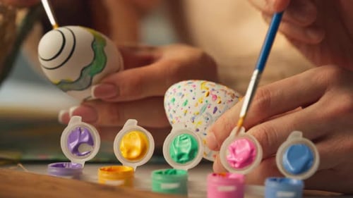 Hände, die Ostereier mit Pinsel und bunten Acrylfarben bemalen. Nahaufnahme
