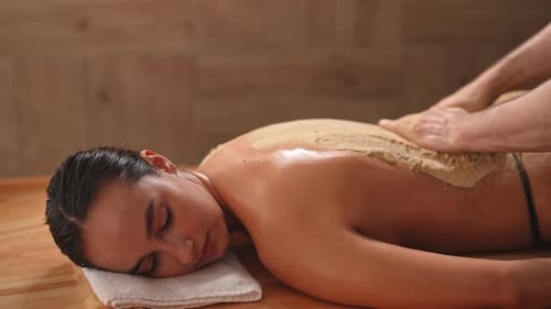 Serene Young Woman Lying Enjoying Back Scrub at Luxury Spa Salon Closeup Hands of Unrecognizable