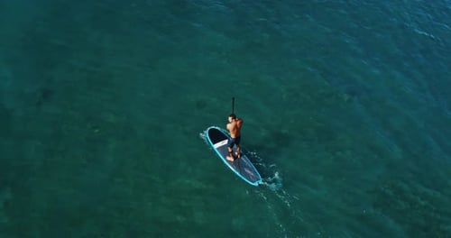 Aerial view of young man stand up paddle boarding on blue ocean waves