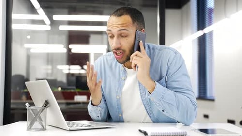 Angry african american businessman arguing talking on mobile phone while sitting in business office.