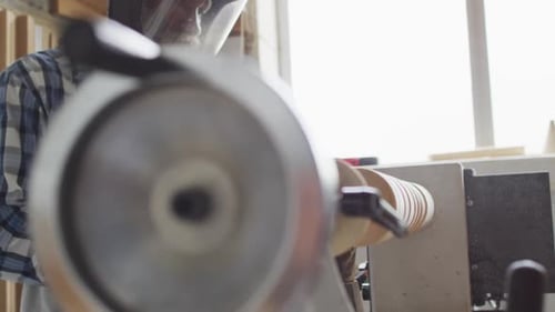 African american male carpenter wearing protective helmet turning wood on a lathe at carpentry shop