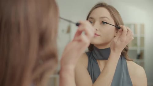 Rückansicht einer hübschen Frau, die vor dem Spiegel Mascara auf die Wimpern aufträgt