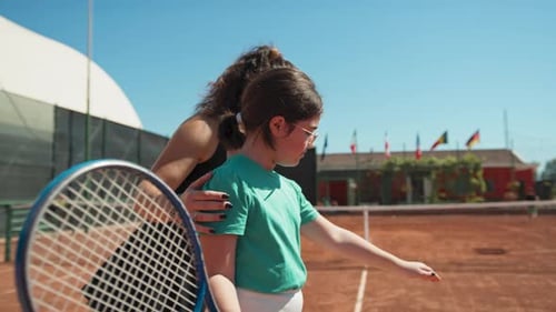 Female Instructor Teaches Little Girl How To Move Tennis Racket In The Field