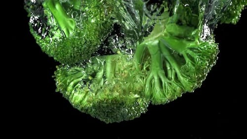 Fresh Broccoli Florets Plunging into Water on Black Background