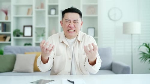 Webcam view. Angry excited asian businessman arguing over video call looking at camera while sitting