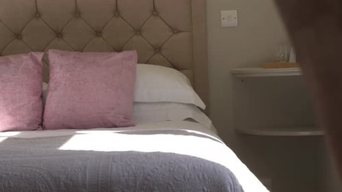 Licht strahlt durch das Hotelzimmerfenster auf ein luxuriöses Landbett mit bequemen rosa Kissen, die für uns bereit sind