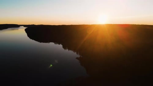 Sunset over Black Silhouetted Forest Next Calm Reflecting Lake AERIAL