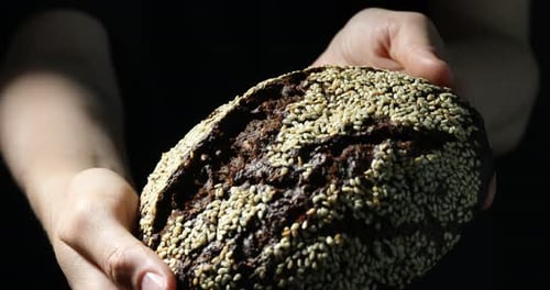 Hands Presenting a Loaf of Fresh Sesame Bread
