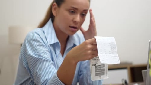 Woman looks worried at receipt in home office