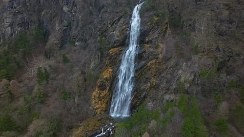 Aerial view of a towering waterfall cascading down a steep, rocky cliff surrounded by lush greenery.