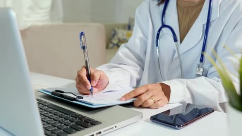 Medical Professional Writes on Documents at Desk