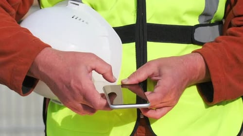 Smartphone en manos masculinas de un constructor escribiendo un mensaje con un casco blanco
