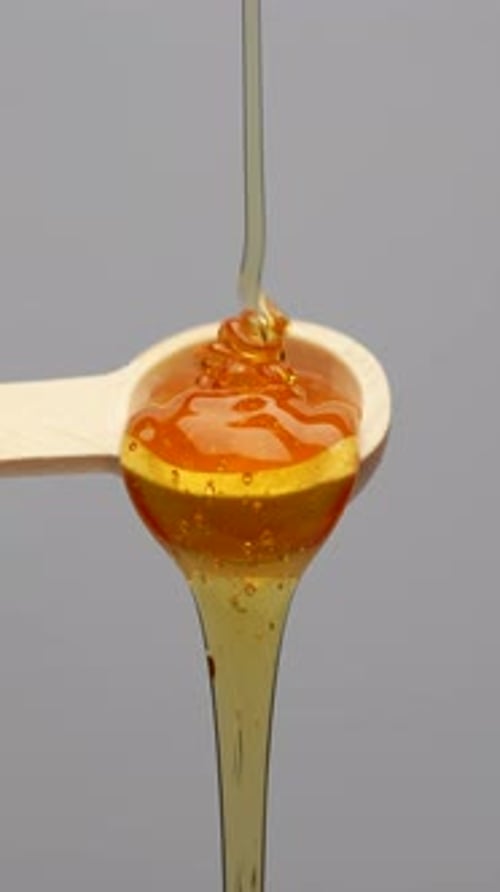 Honey Pouring onto Wooden Spoon