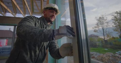 Worker examines window frame for precise alignment in residential construction site, quality