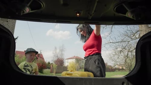Woman Packs Suitcase into Car Trunk with Child Watching