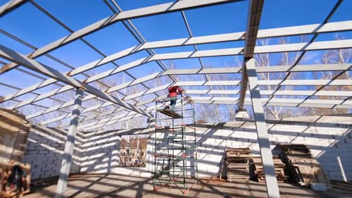 Man in red jacket stands on the scaffolding using instrument.