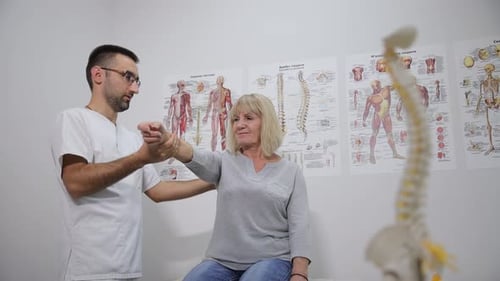 Doctor examines senior woman's arm in clinic