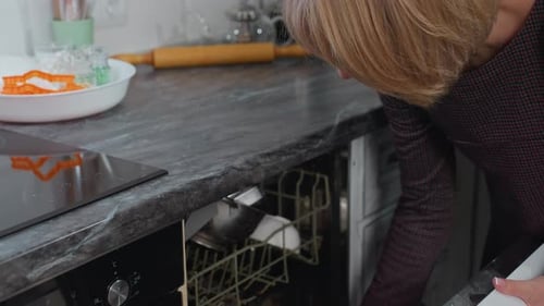 Woman Loading Pot into Dishwasher in Kitchen