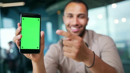 Close up of smartphone with green screen showing young businessman sitting in modern office.