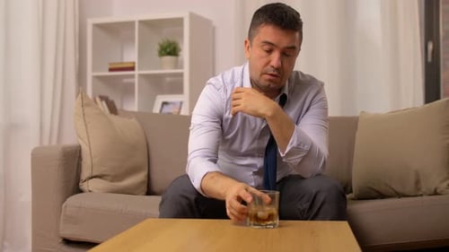 Man With Untied Tie Drinks Liquor on Couch