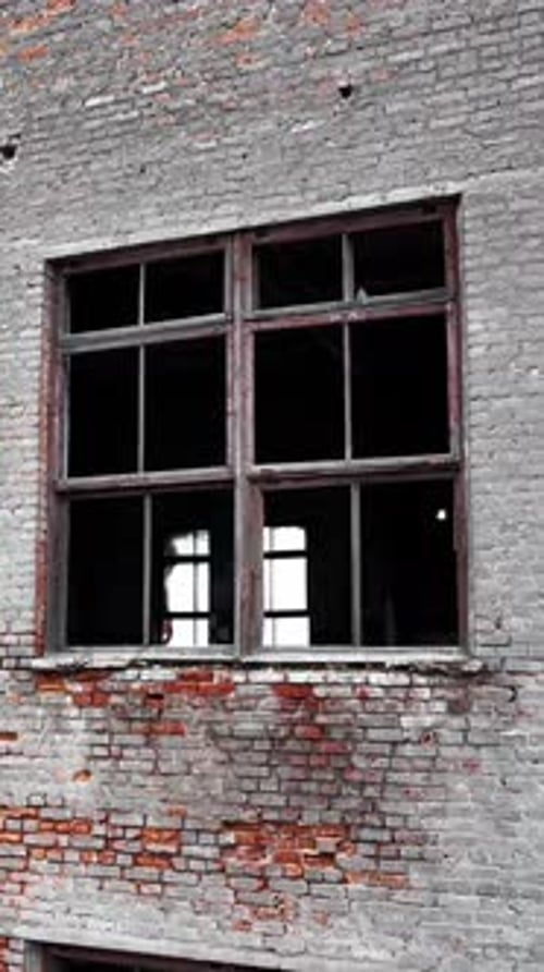 Forlorn building with crashed windows. Approaching to the brick wall of the construction.