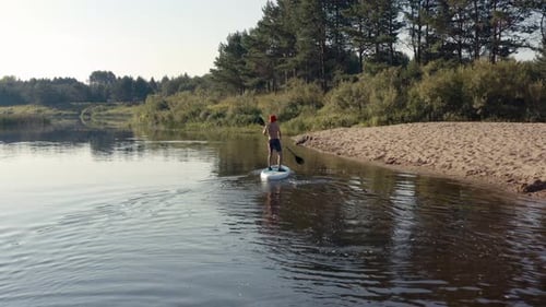Man Paddleboarding on River Near Sandy Shore