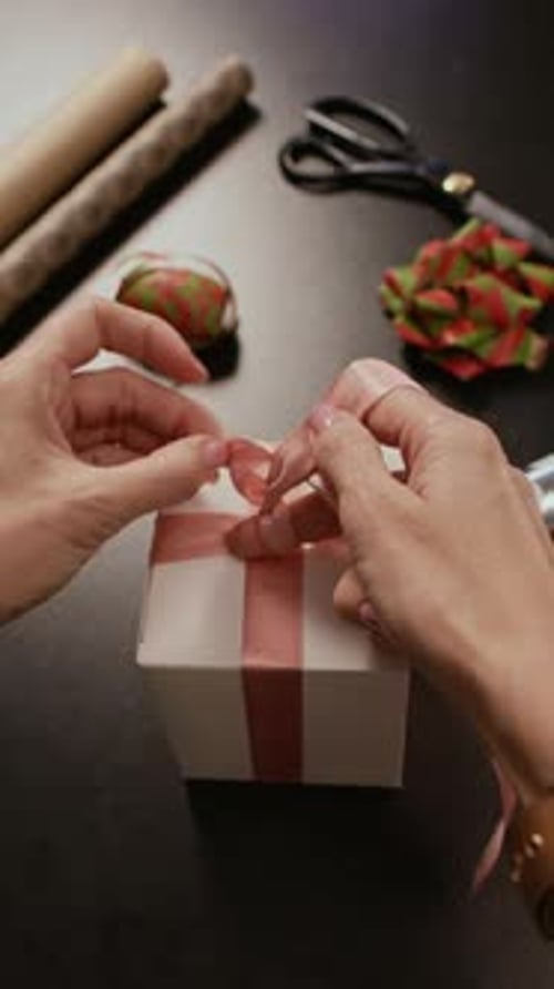 Woman Tying Pink Ribbon on Small White Gift