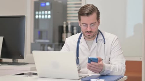 Doctor with Smartphone Working at Desk
