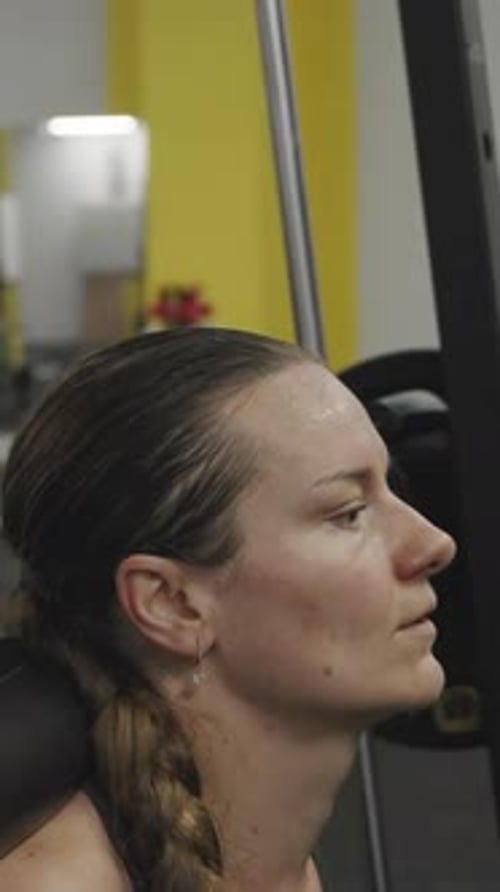 Vertikales Video. Junge Frau trainiert fleißig im Fitnessstudio und macht Kniebeugen
mit einer Langhantel