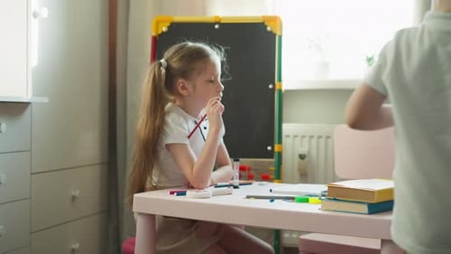 Girl Drawing at Table with Brother Next to Her