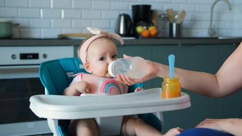 Baby Drinking Bottle While Sitting in High Chair