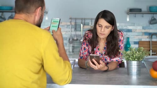 Couple Using Smartphones at Kitchen Counter