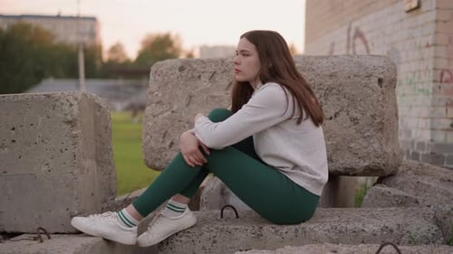 Lady Sits on Concrete Rocks Near Building
