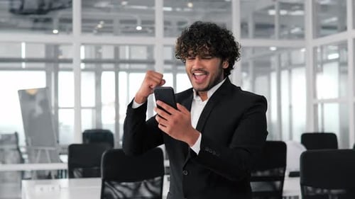 Young Adult Looks at Phone and Celebrates Win