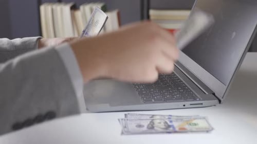 Man Types on Laptop and Organizes US Currency