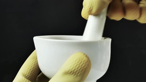 Des mains gantées travaillant avec précision avec un mortier en porcelaine, mettant en valeur la composition de formules dans un