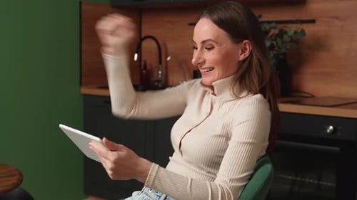 Woman Celebrates Success While Using Tablet at Home