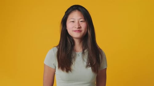 Young woman looking at camera showing thumbs up isolated on yellow background in studio