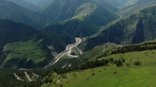 Curvy Mountain Roads Cutting Through Lush Green Hillsides Leading to a Small Village in the Valley