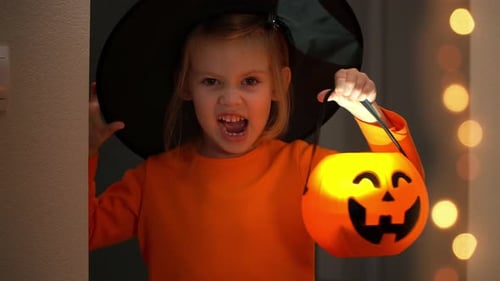 Halloween Angry Girl in Witch Costume Scares with Lantern Pumpkin in Dark