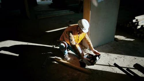 Trabalhador da construção civil se senta perto da parede e abre a caixa de ferramentas no canteiro de obras