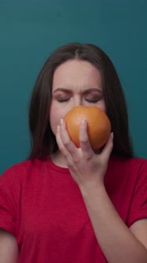 A Young Woman Joyfully Holds a Fresh Orange Close to Her Face Radiating Happiness and Beauty
