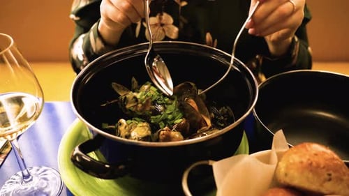the shot of a woman eating hot mussels from black bowl in restaurant