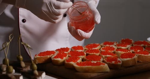 Chef making sandwiches with red caviar for buffet at table indoors, closeup