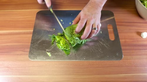 Close-up of a person slicing fresh green salad on a stainless-steel cutting board in a home kitchen.