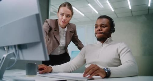 Afroamerikanischer Mann mit Headset und kaukasische Frau, die am Computer in einem modernen Büro arbeitet