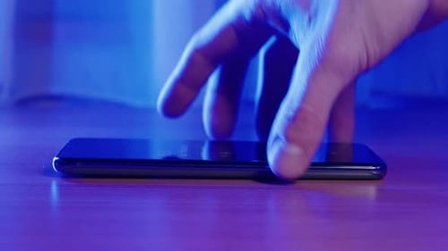 Closeup Of Young Man Hands Pick Up Phone From Desk Blue Background. Smart Phone Macro Close Up.