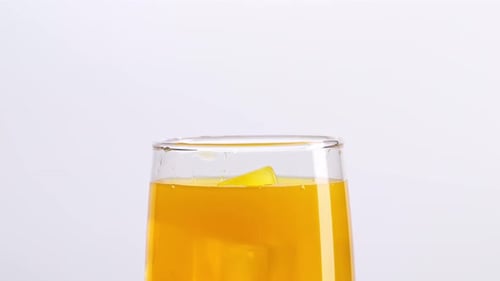 Close Up Of Ice Cubes Falling In A Glass Of Orange Juice On The Light White Screen Background